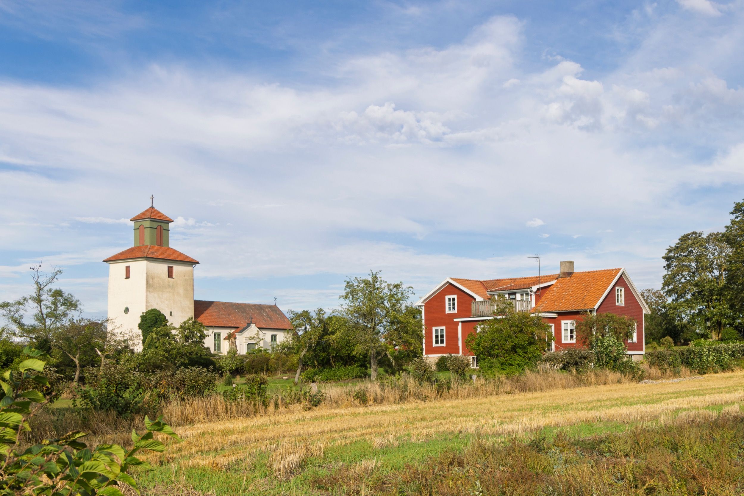 Die weiße Kirche von Resmo in idyllischer Landschaft mit charakteristischem roten Bauernhof auf Öland.